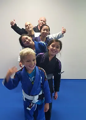 Kids and coaches from GT BJJ stacked in a line on the blue mats, thumbs up