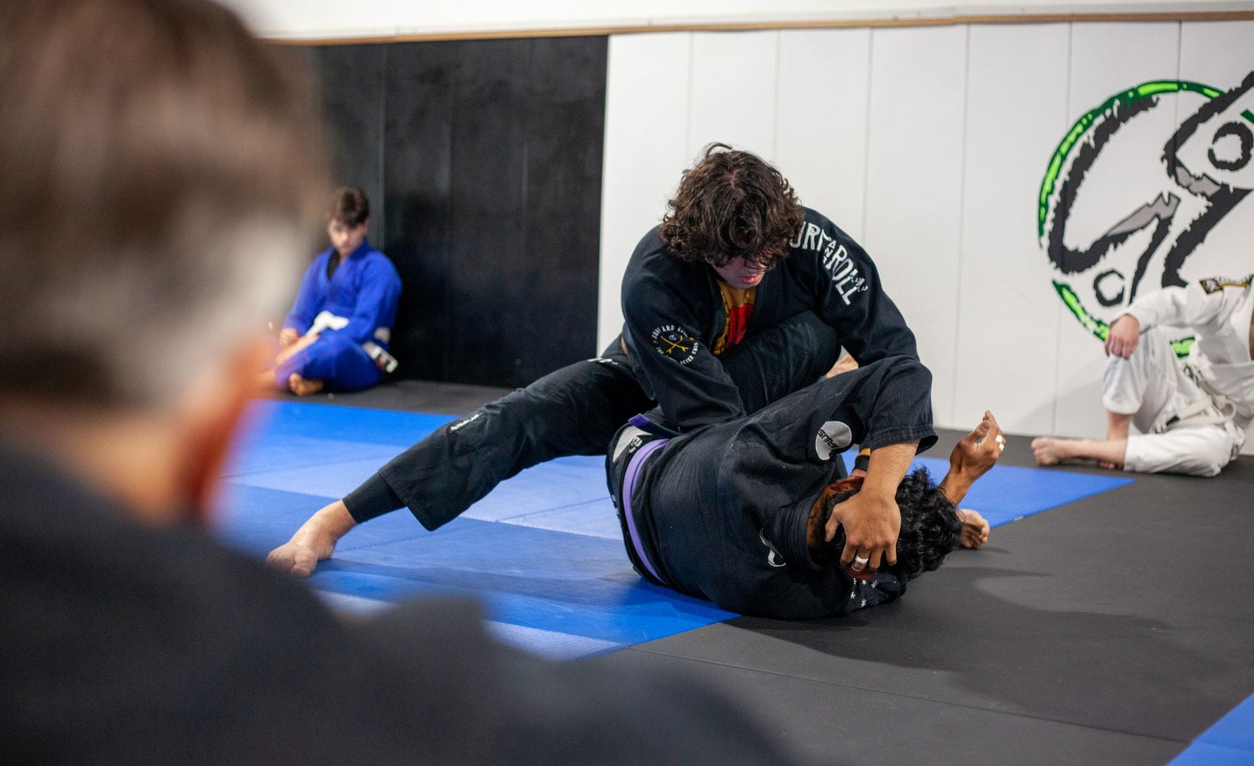 Two grapplers in black gis fighting for top position on the mats